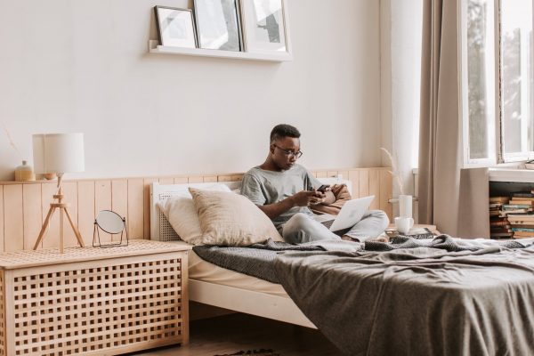 student on a bed browsing with a cup of tea by the side 